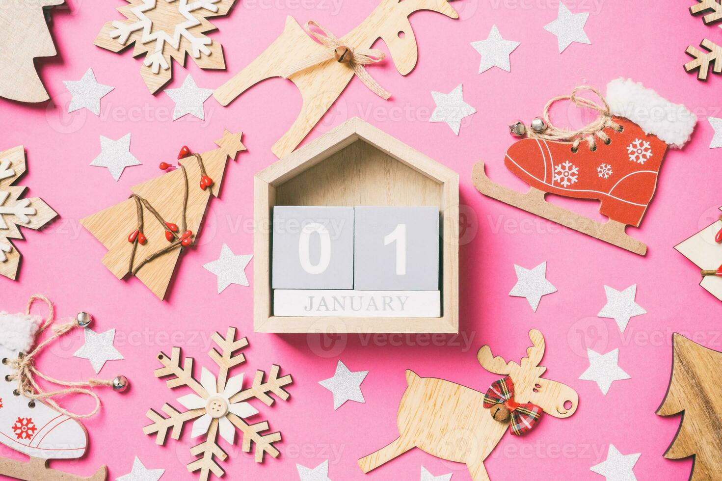 Top view of calendar, pink background decorated with festive toys and Christmas symbols reindeers and New Year trees. The first of January. Holiday concept photo