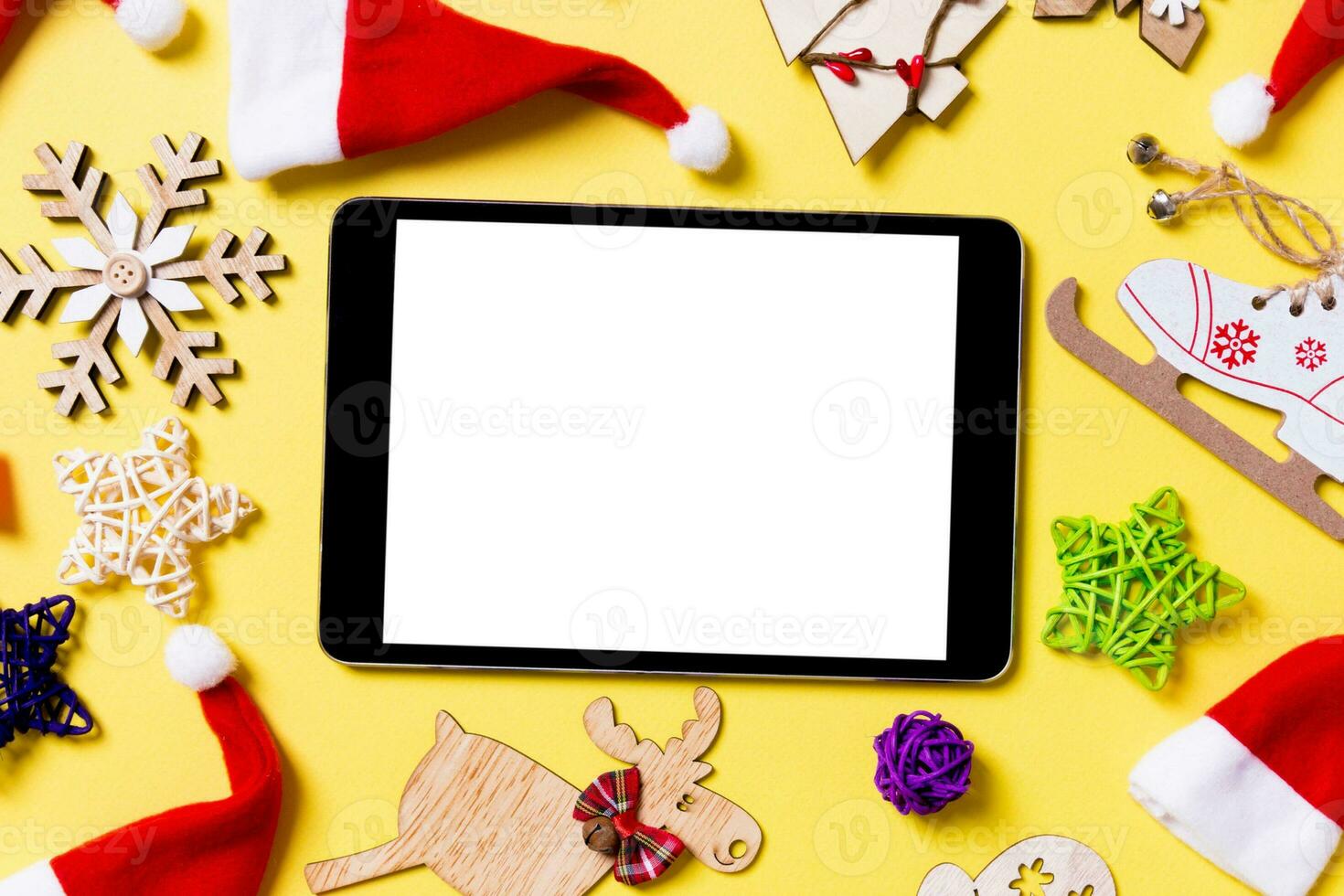 Top view of digital tablet with Christmas decorations and Santa hats on yellow background. Happy holiday concept photo