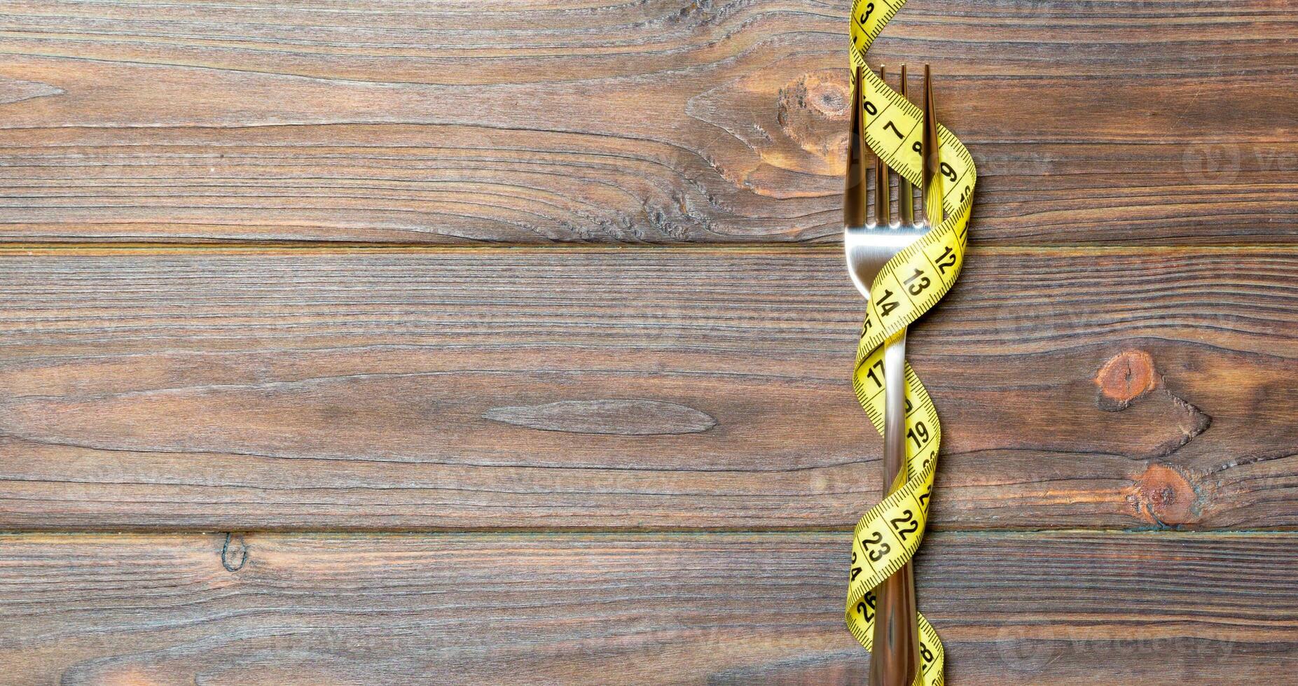 Top view of wrapped fork in tape measure on wooden background. Healthy eating and diet concept photo