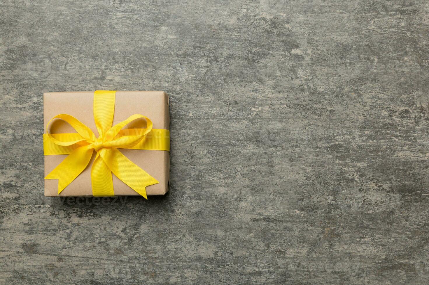 Holiday gift box wrapped in craft paper with colored bow on table background. Top view, flat lay, copy space photo