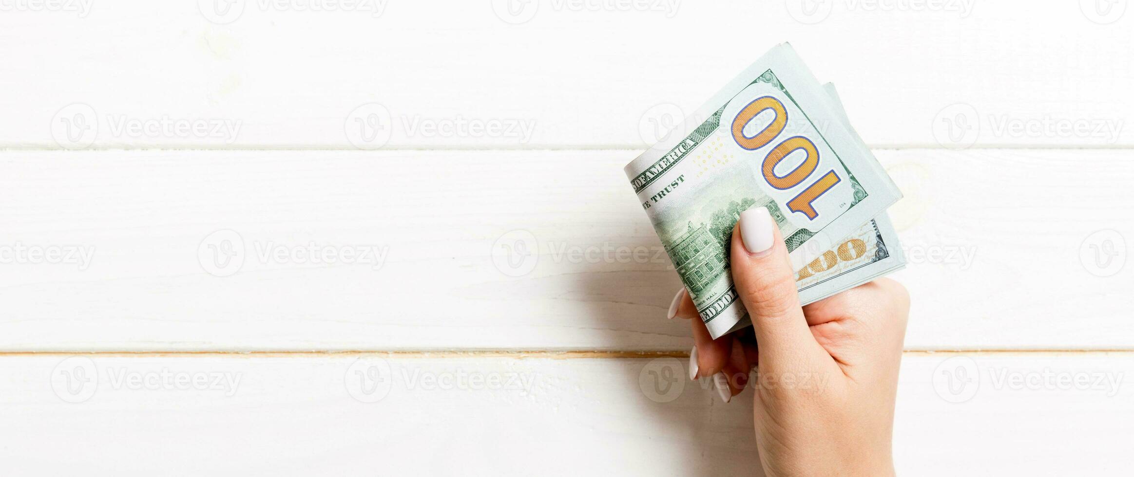 Top view of female hand holding a pack of money on wooden background. One hundred dollars. Business concept with empty space for your design. Charity and tips concept photo
