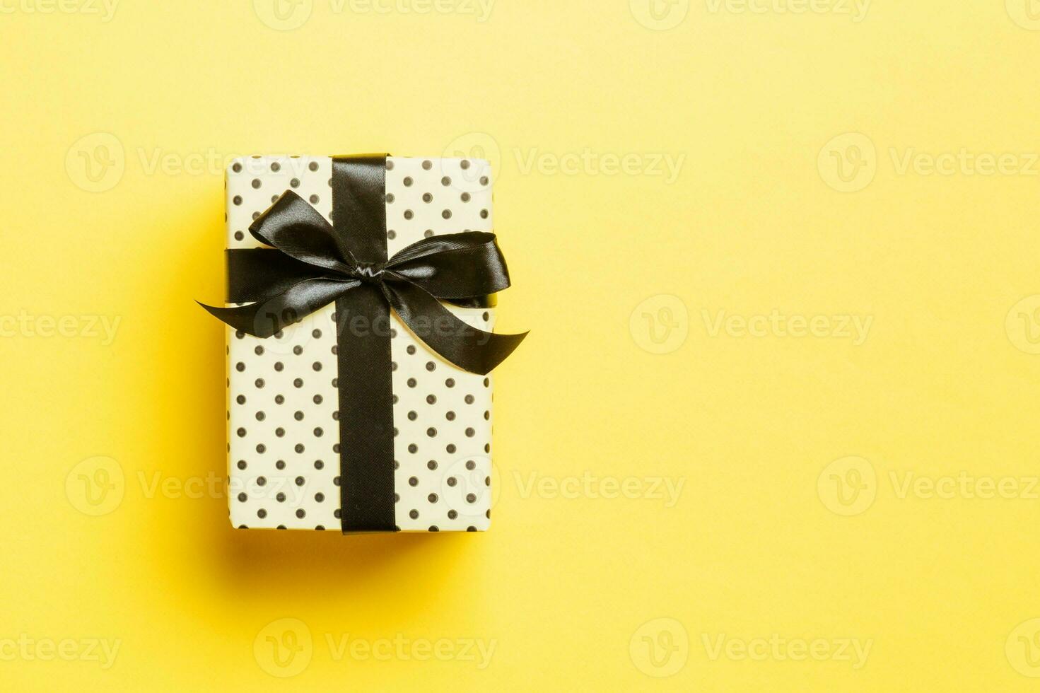 wrapped Christmas or other holiday handmade present in paper with black ribbon on yellow background. Present box, decoration of gift on colored table, top view with copy space photo