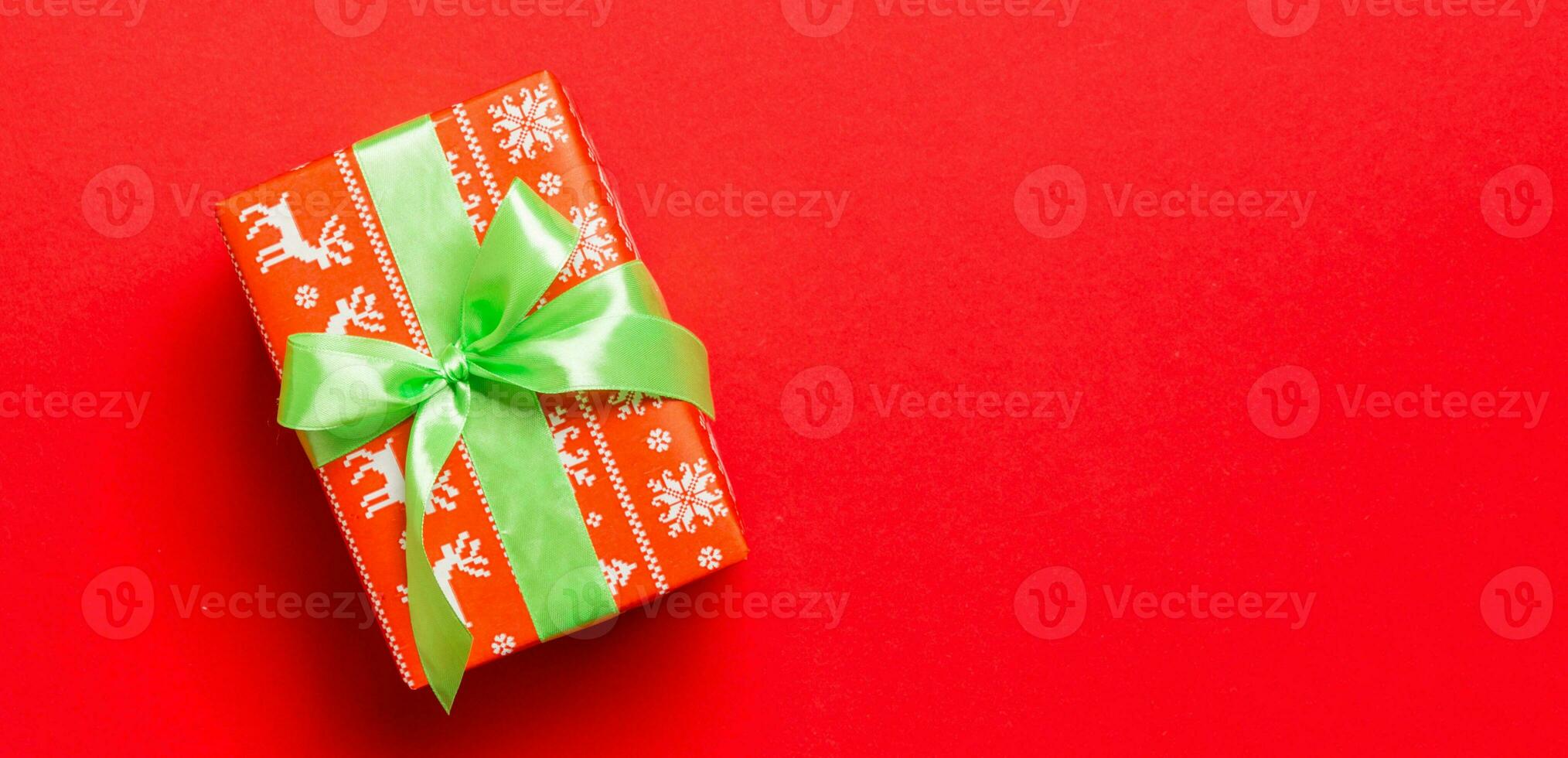 Gift box with green bow for Christmas or New Year day on red background, top view with copy space photo