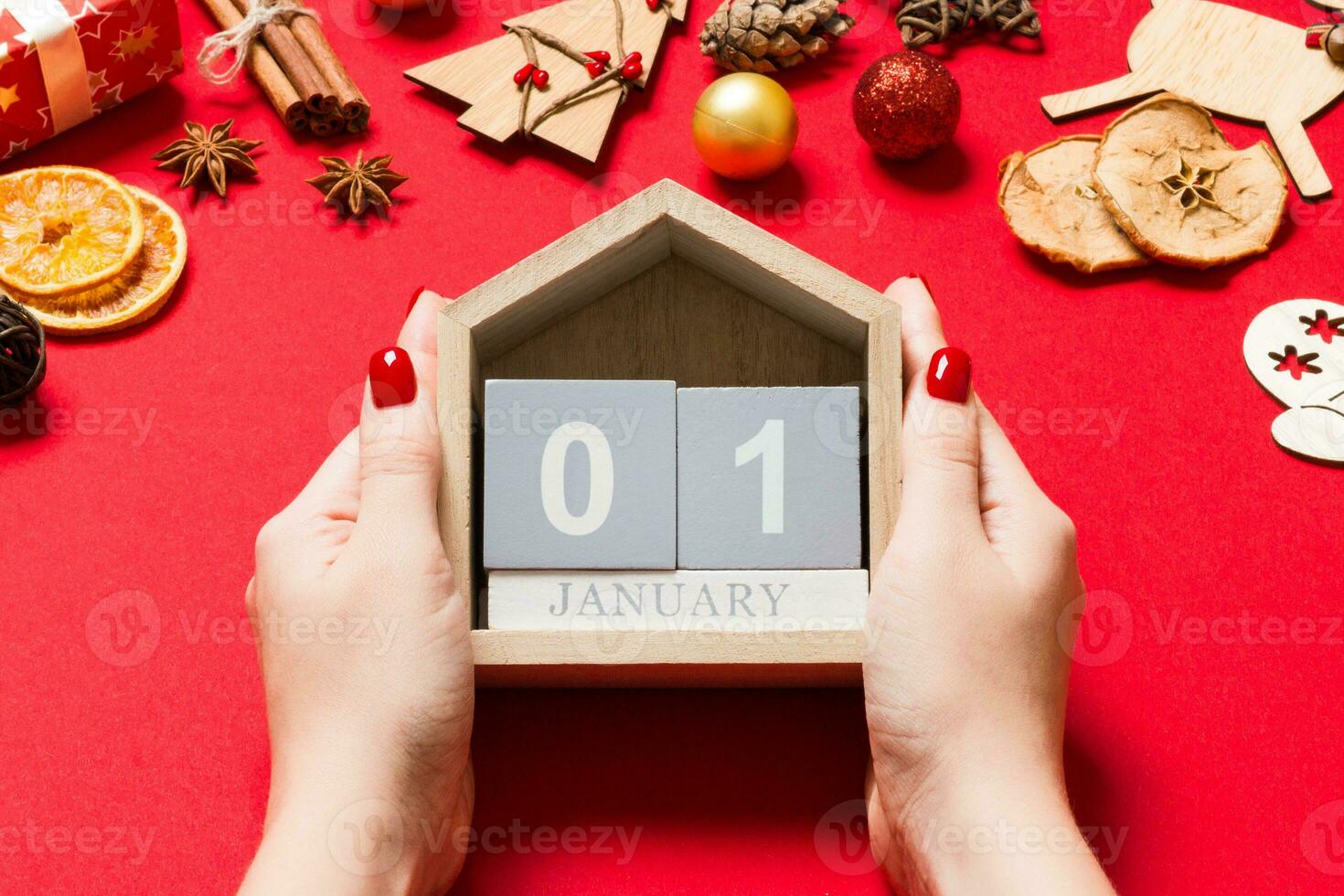 Top view of female hands holding calendar on red background. The first of January. Holiday decorations. New Year concept photo