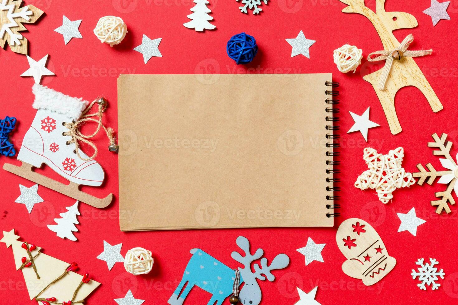 Top view of notebook, holiday toys and decorations on red Christmas background. New Year time concept photo