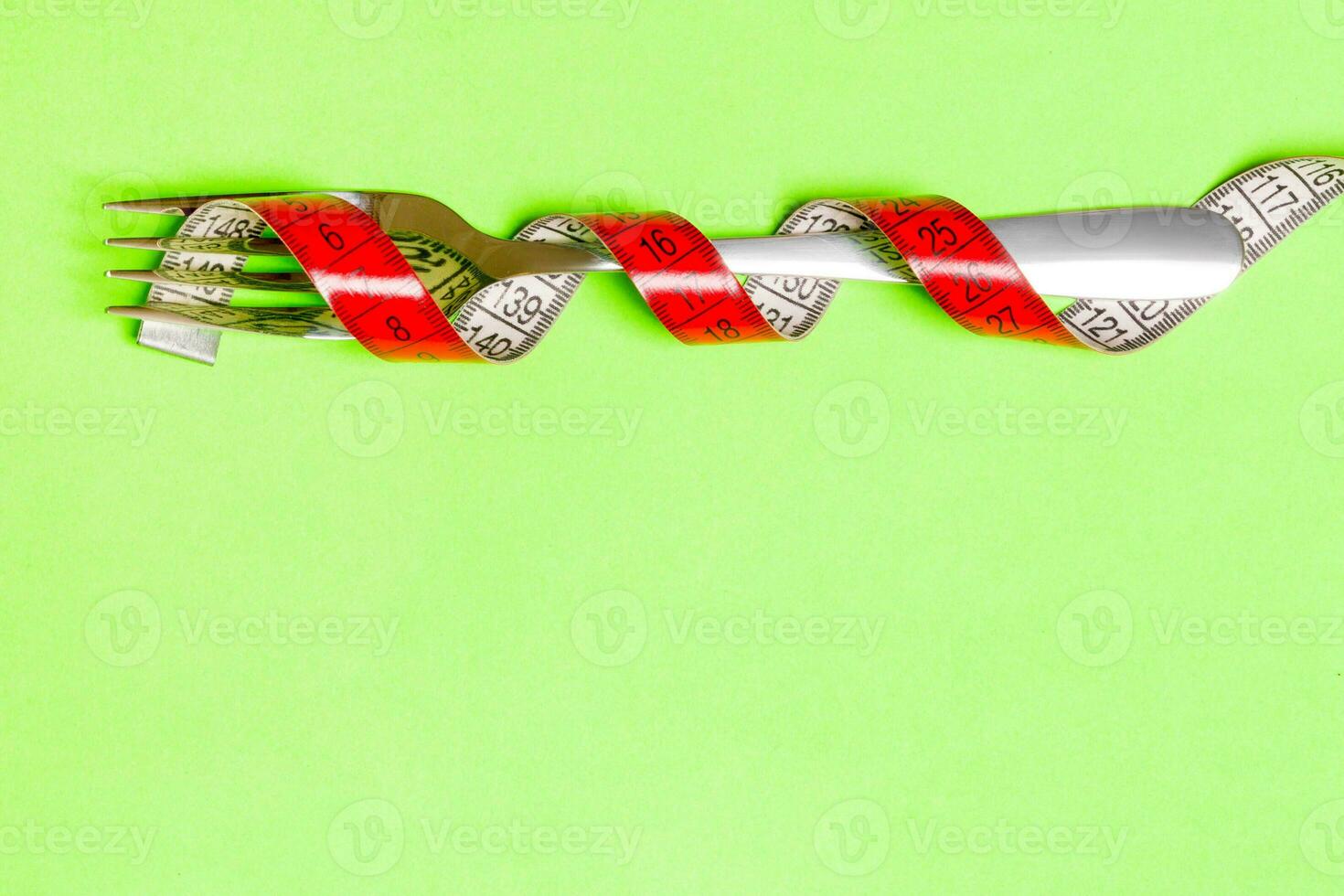 Close up of fork wrapped with tape measure on green background. Top view of obesity concept photo