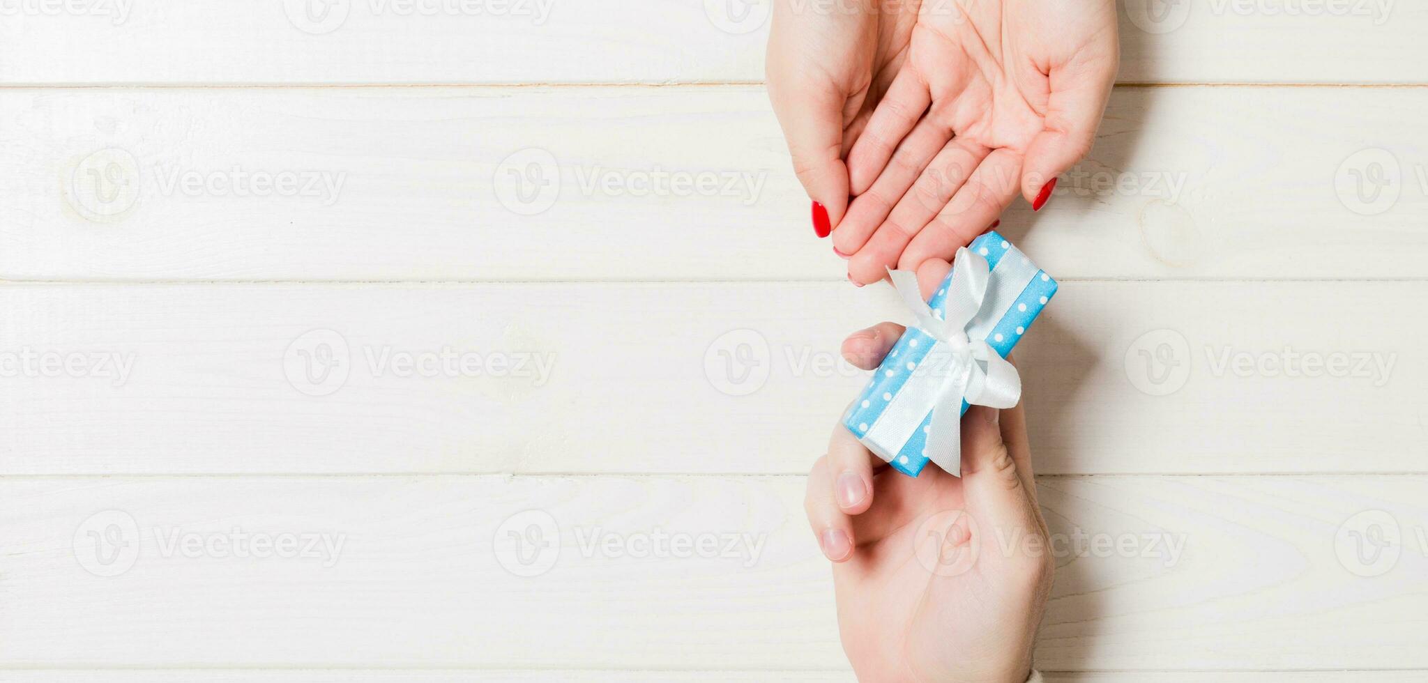 Top view of a present in male and female hands on wooden background. Congratulating of each other concept. Copy space photo