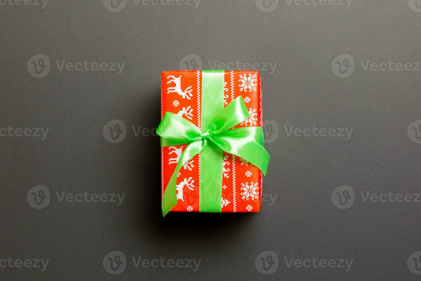 wrapped Christmas or other holiday handmade present in paper with green ribbon on black background. Present box, decoration of gift on colored table, top view with copy space photo