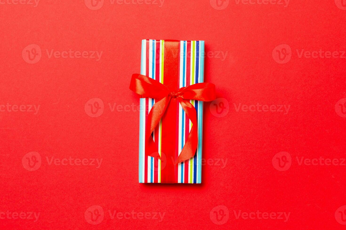 Gift box with red bow for Christmas or New Year day on red background, top view with copy space photo