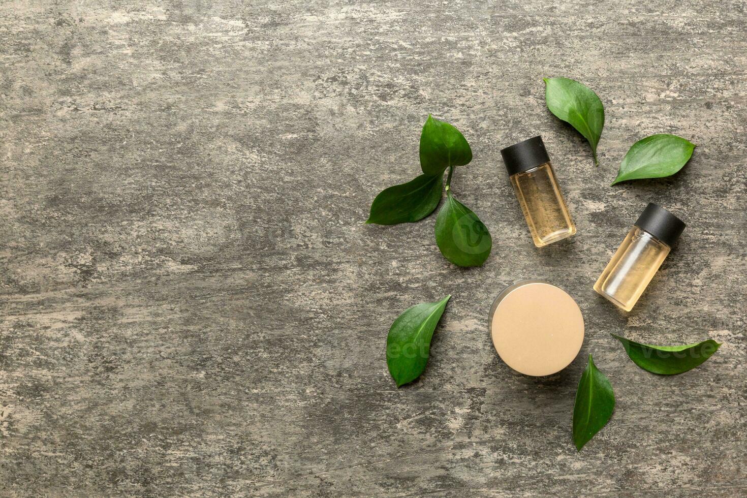 Organic cosmetic products with green leaves on cement background. Copy space, flat lay photo