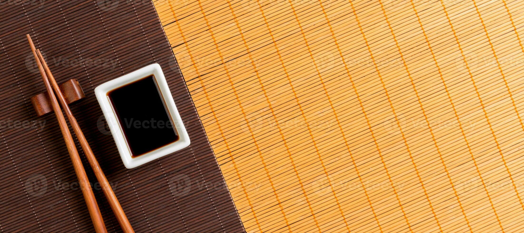Chopsticks and bowl with soy sauce on two bamboo mat blak and yellow top view with copy space photo