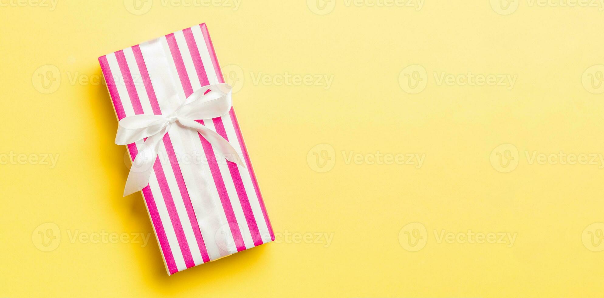 Top view Christmas present box with white bow on yellow background with copy space photo