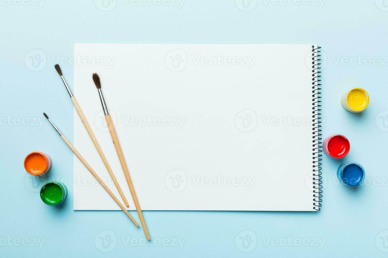 Album pages and paints, pencils, brush on a colored background. Top view with empty space. workplace for creativity. home teaching concept drawing photo