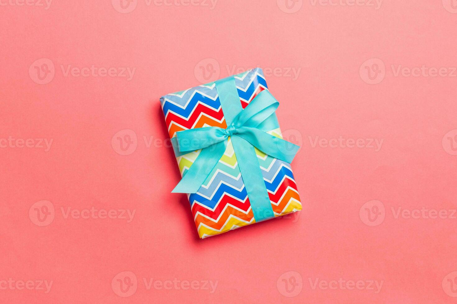 wrapped Christmas or other holiday handmade present in paper with blue ribbon on living coral background. Present box, decoration of gift on colored table, top view with copy space photo