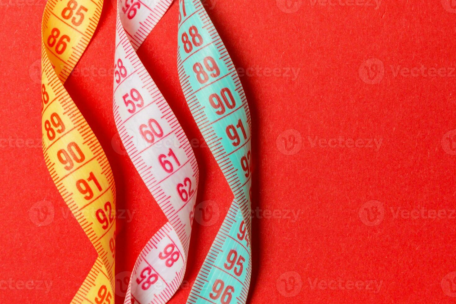 Top view of spiral colorful measure tapes on red background. Concept of perfect female figure with empty space for your idea photo