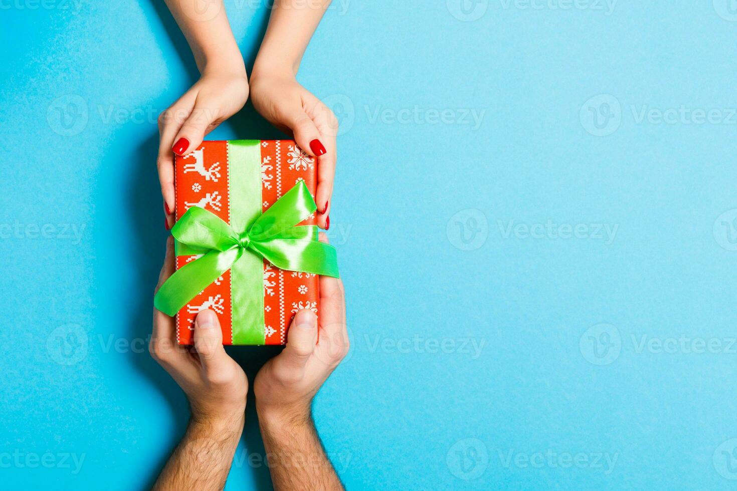 Top view of two people sharing a present on colorful background. Holiday and surprise concept. Close up photo