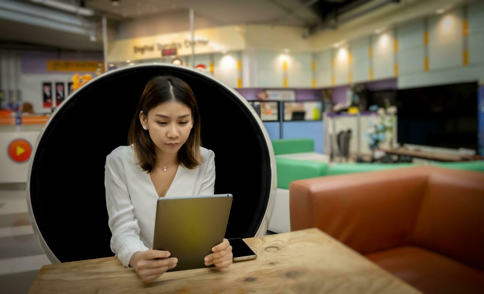 Beautiful asian businesswoman is having a meeting with her boss through a tablet with a serious expression while sitting in a modern round chair in the living room. photo