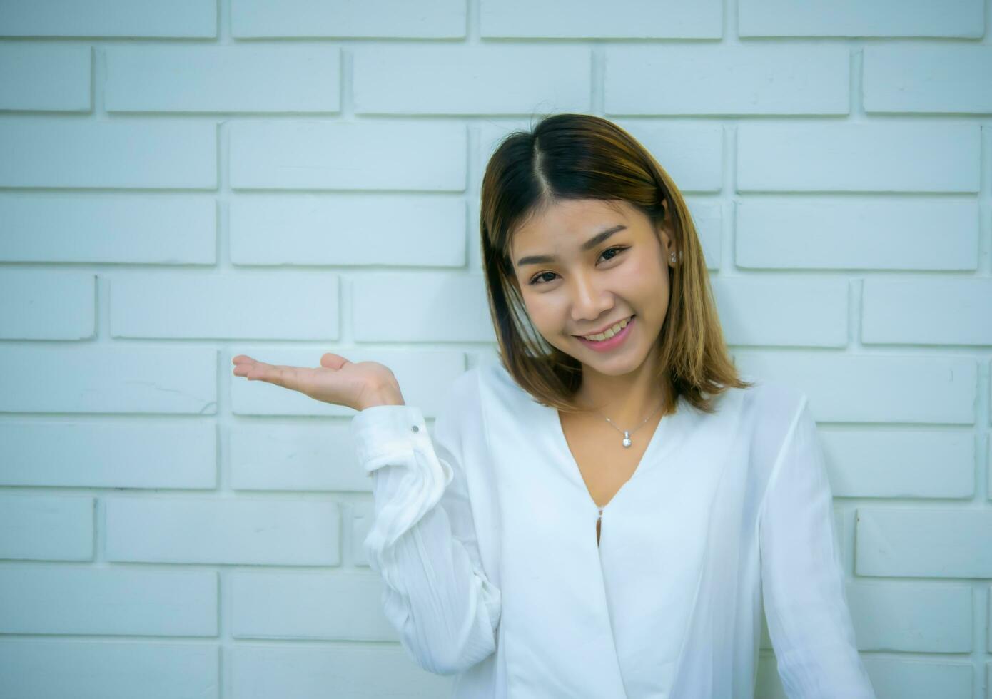 hermosa asiático negocio mujer en pie con un sonrisa mientras mirando a el cámara en contra un blanco ladrillo fondo, digital marketing. foto