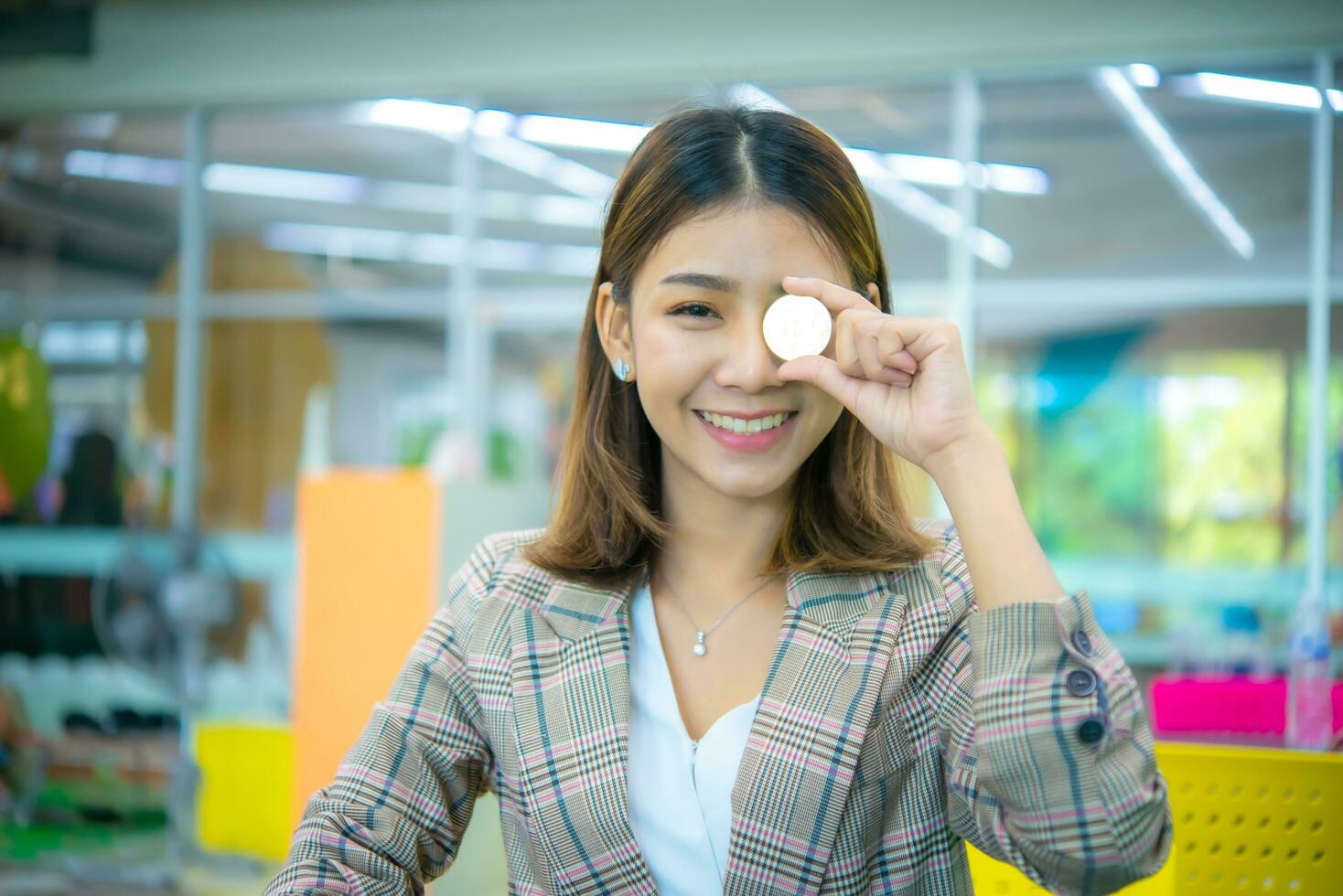 Beautiful asian business woman hold a coin in her one hand and covered on her eyes while looking to the camera with a smile on her face. photo