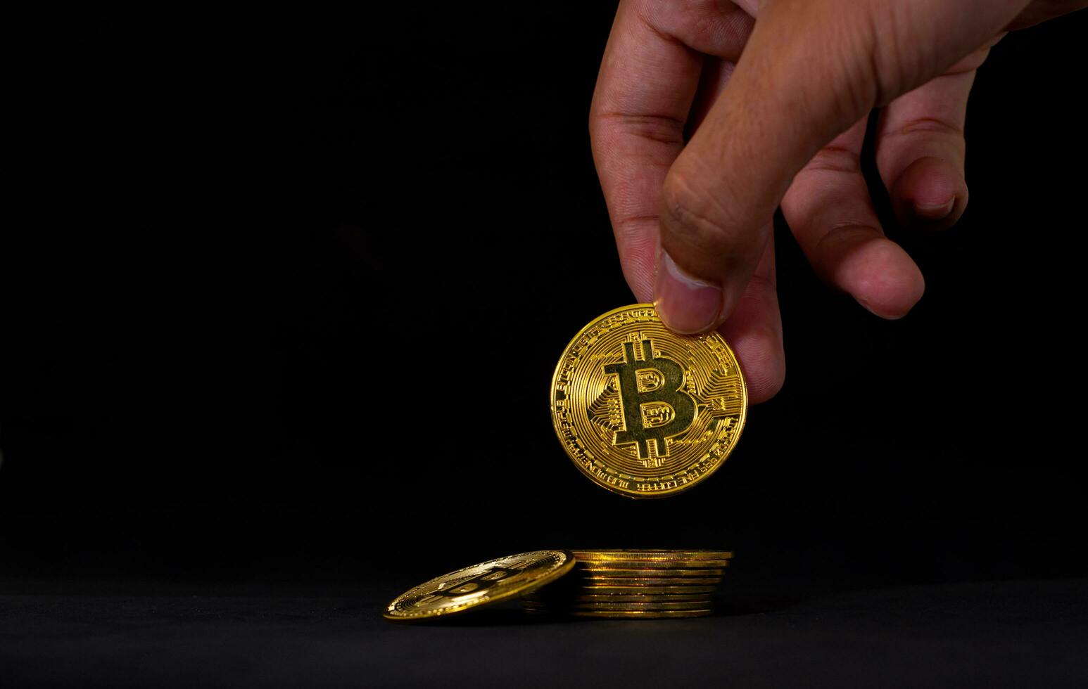 Hand holding bitcoin from stack, Bitcoin on black table with black background. photo