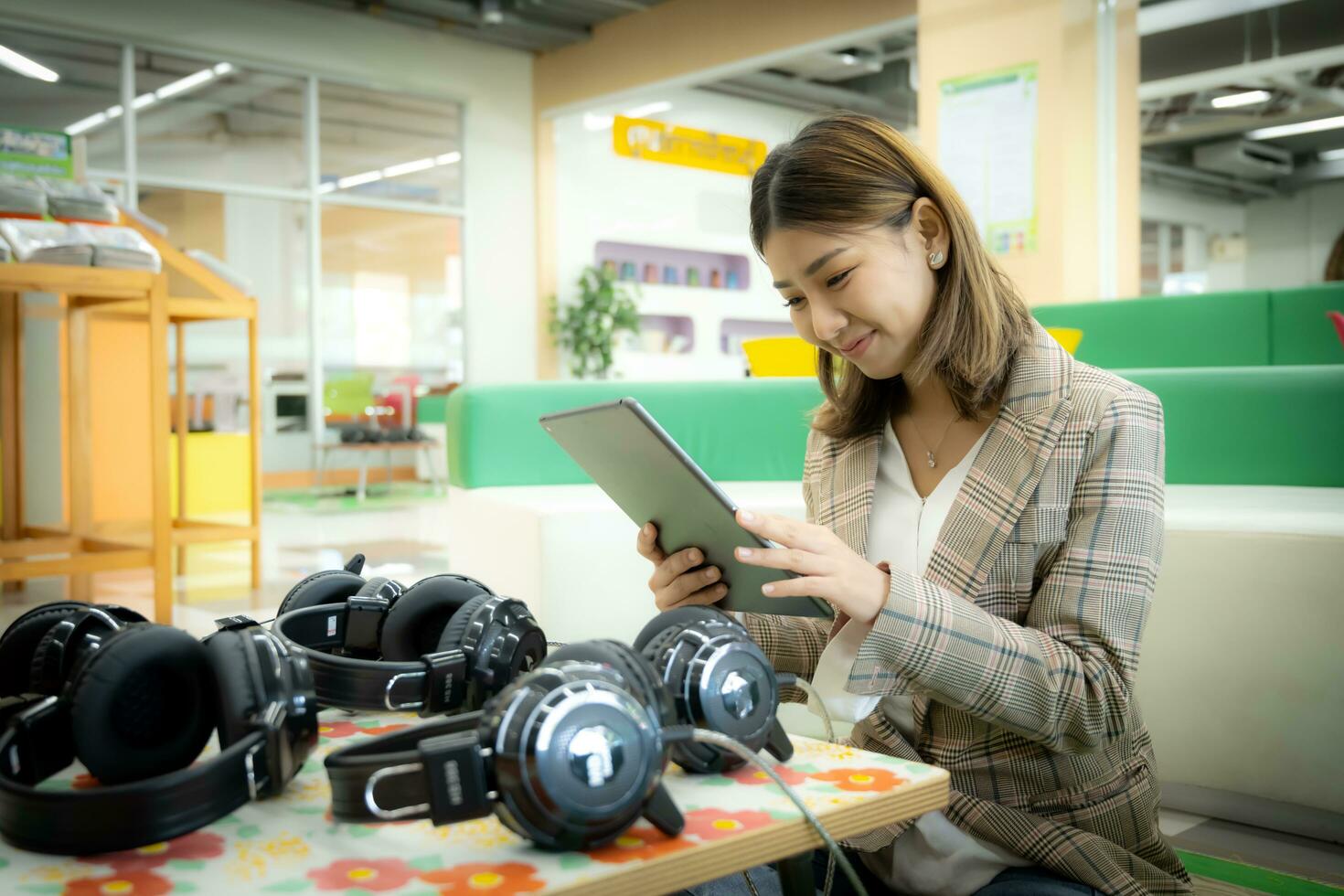 Beautiful asian businesswoman is sitting and  presses tablet to promote her headphone product with smile on her face, Marketing concept. photo