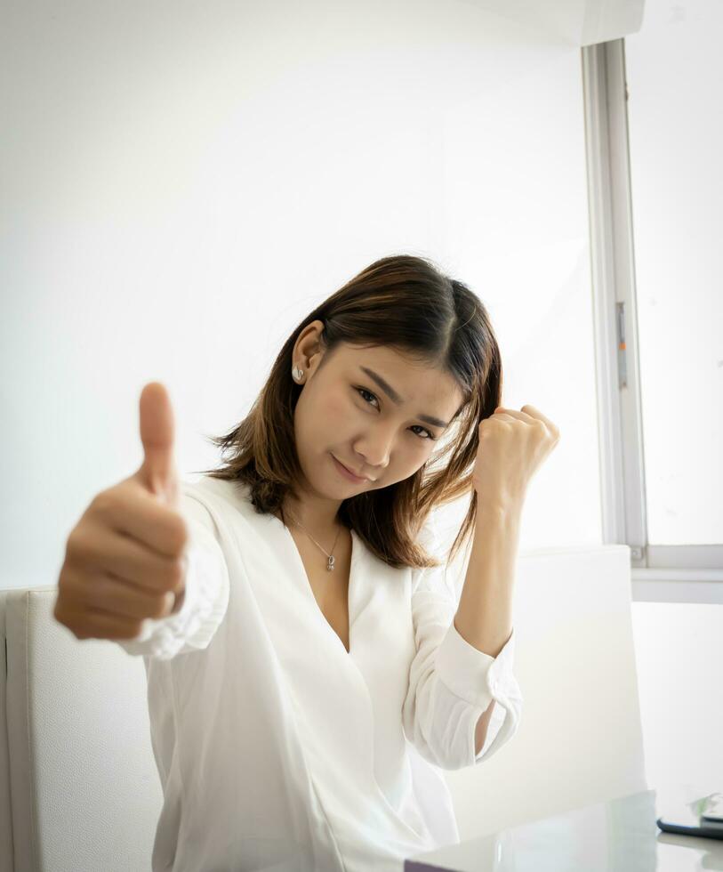 Vertical picture of cheerful beautiful asian businesswoman thumbs up to the camera with smile on her face. photo