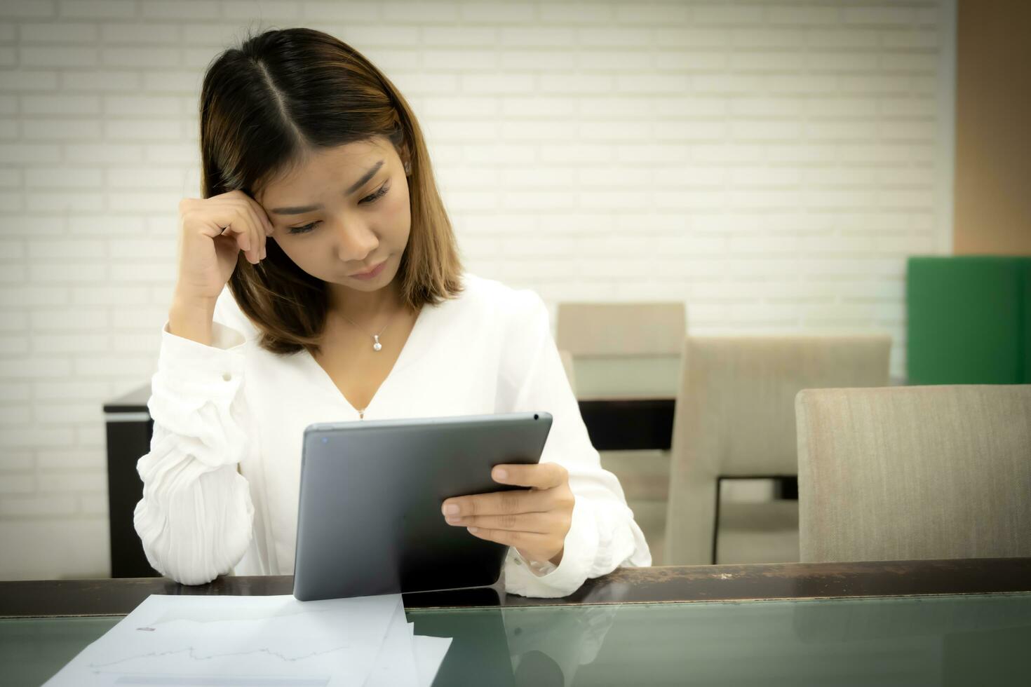 Beautiful asian female teacher sitting and looking down goes to the tablet with a serious expression on her desk. photo