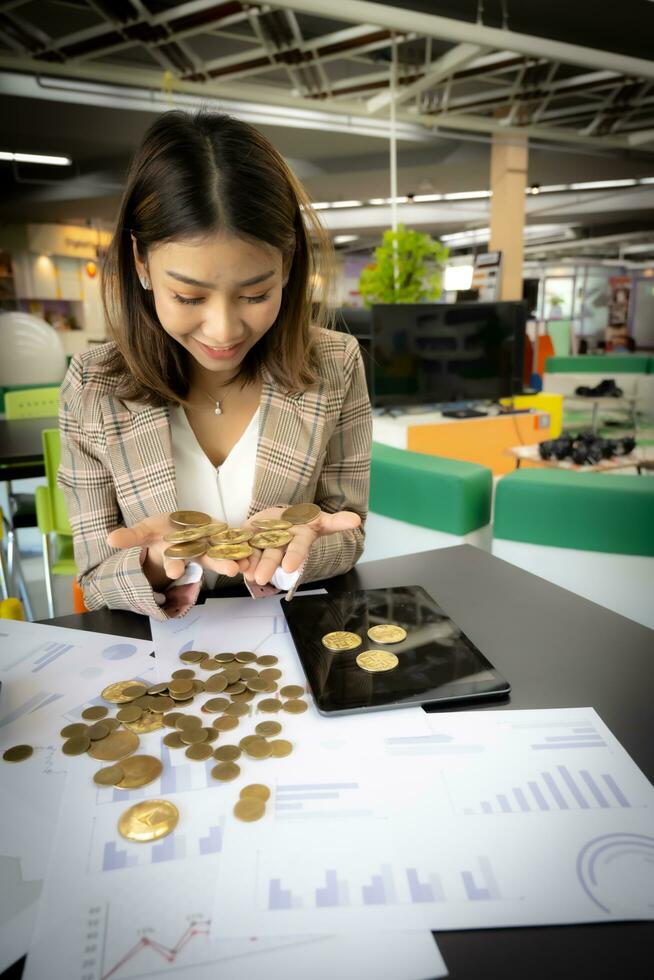 Vertical picture featuring a successful asian businesswoman is showing her own bitcoins with a smile on her face in her office. photo