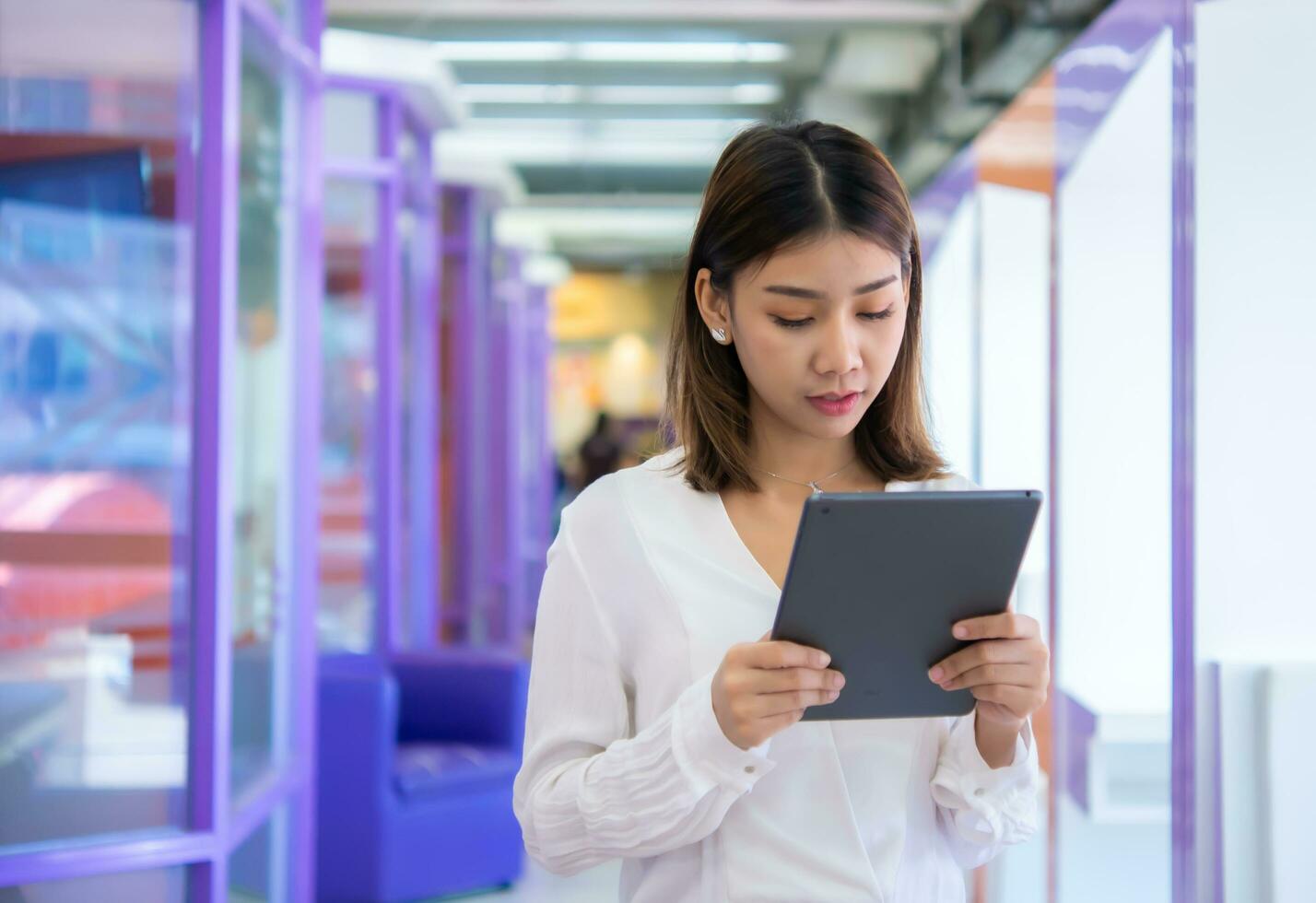 Beautiful asian business woman is standing and looking down at her tablet with a suspect expression, Digital marketing. photo