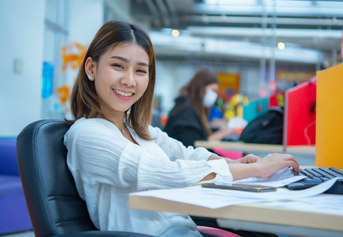 hermosa asiático negocio mujer es sentado en su oficina, sonriente y mirando a el cámara con felicidad, digital marketing. foto