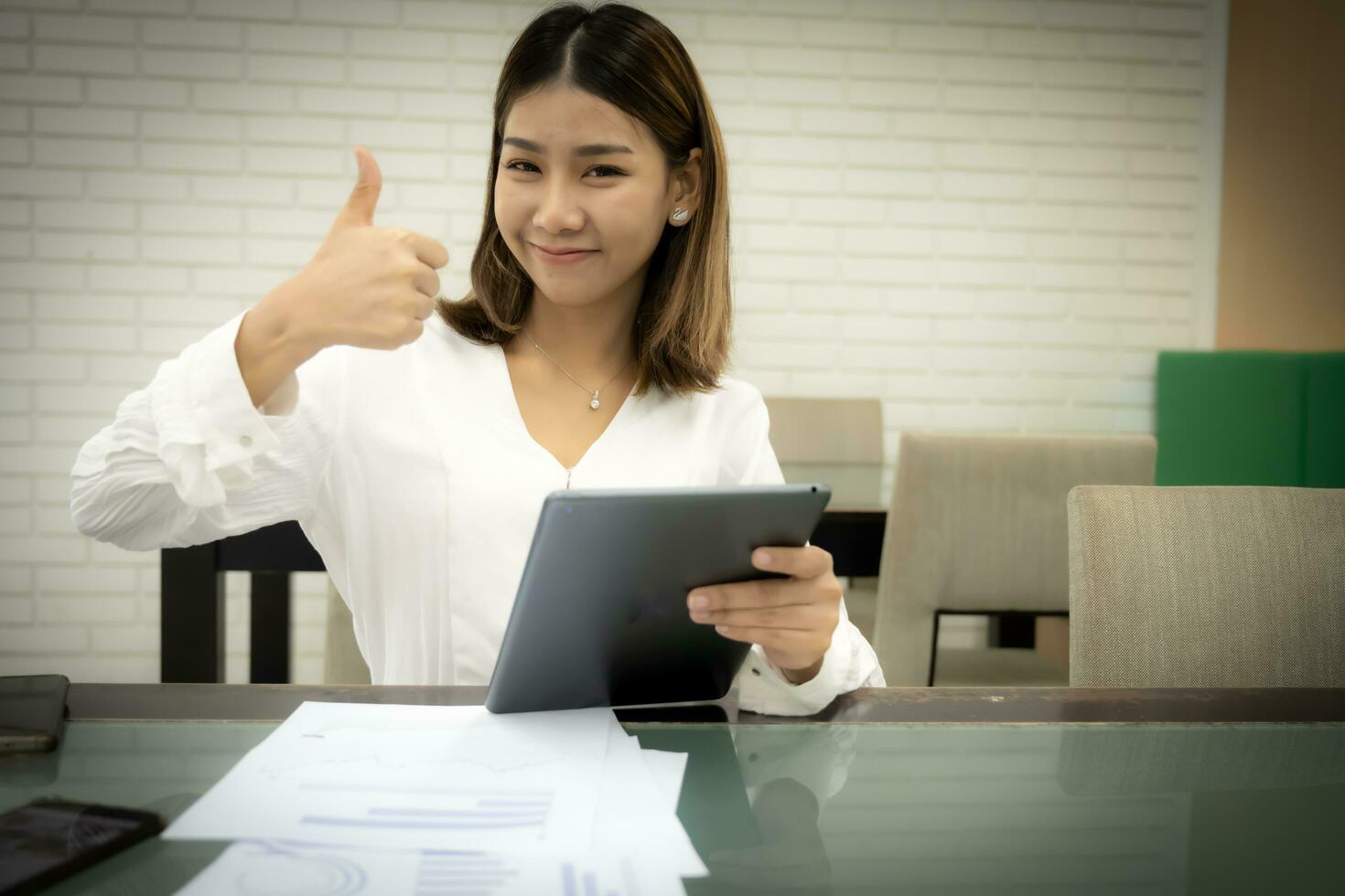 Beautiful asian office girl is make sales in online store while holding tablet and thumbs up with smile on her face. photo
