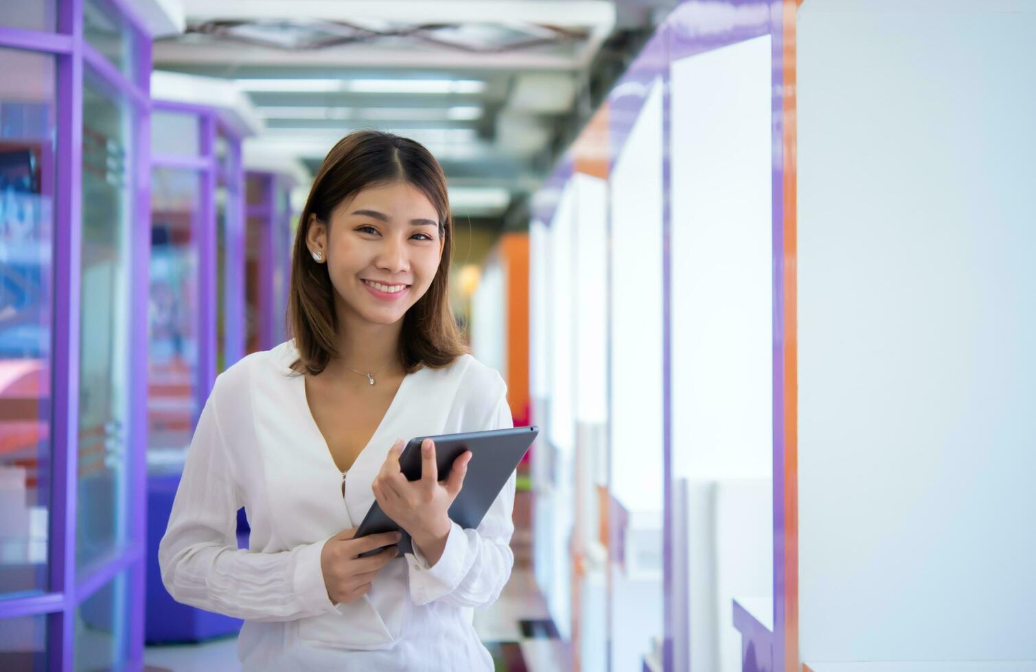 hermosa asiático negocio mujer es en pie frente a el cámara mientras con confianza participación un tableta y sonriente, Copiar espacio, digital marketing. foto