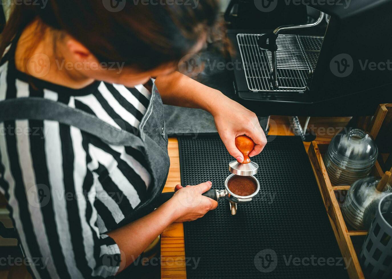 Barista holding portafilter and coffee tamper making an espresso coffee in cafe photo
