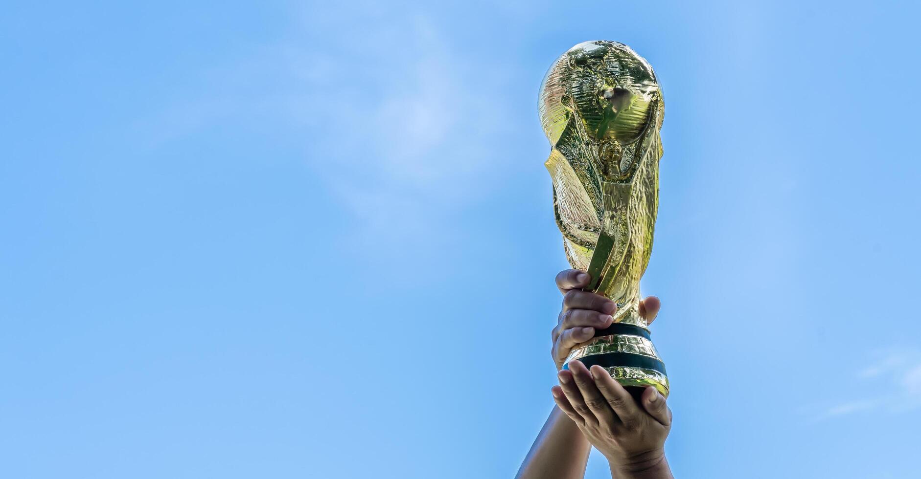 World Cup with background blue sky. hand holding a World Cup winner trophy. The concept for World Cup in Qatar. Copyspace on left for design or text photo