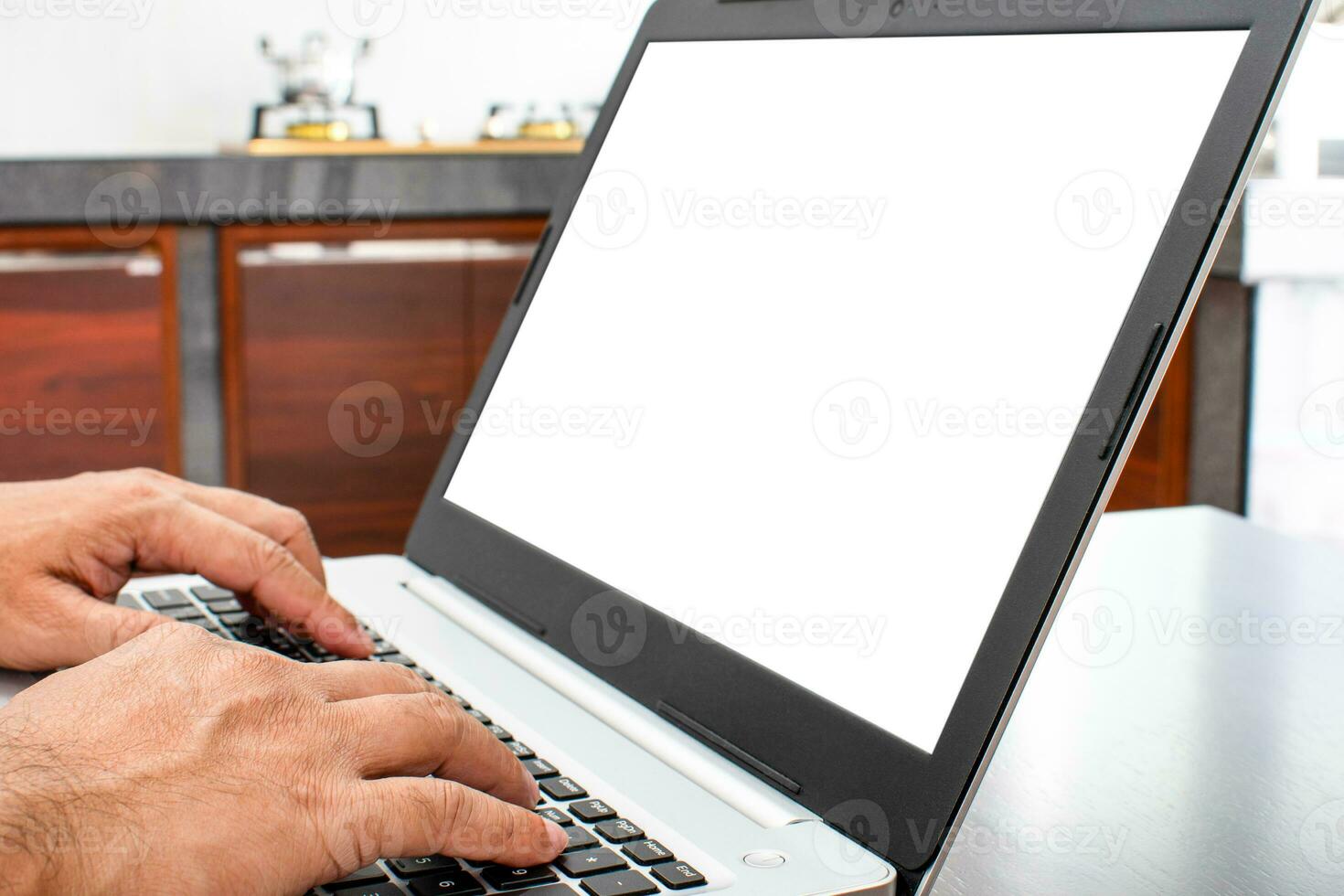 de cerca, un del hombre mano es mecanografía en un ordenador portátil teclado a buscar fuera cómo a cocinar. cuaderno computadora blanco pantalla en el mesa. tiene un maceta en el gas cocina. borroso fondo, burro arriba, recorte camino foto