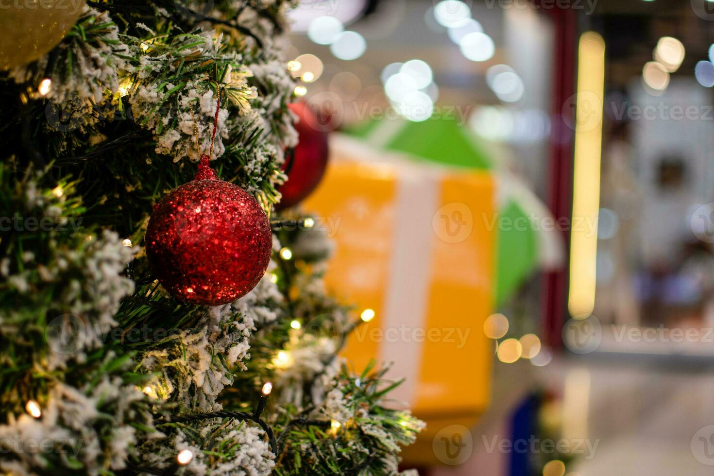 Closeup medium red balls Christmas tree decorated with small bulbs is beautiful. Christmas tree decoration with white snow, copy space on right for design or text, blurred background, beautiful bokeh. photo