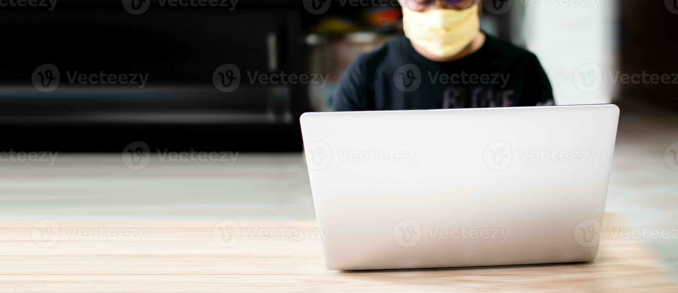The masked man was working at home using a laptop, communicating via the internet with a customer during the coronavirus or COVID-19 outbreak, and as a preventive measure. copy space on left put text photo