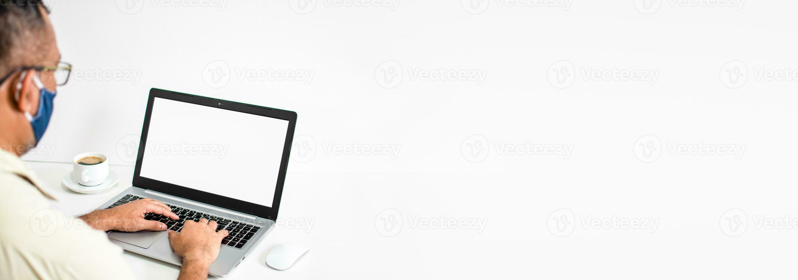 Take a close-up of male hands and laptop with a white blank screen. Young man wearing a mask. Mock-up of a notebook computer monitor. Copyspace on right for design or text. White and Blur background. photo