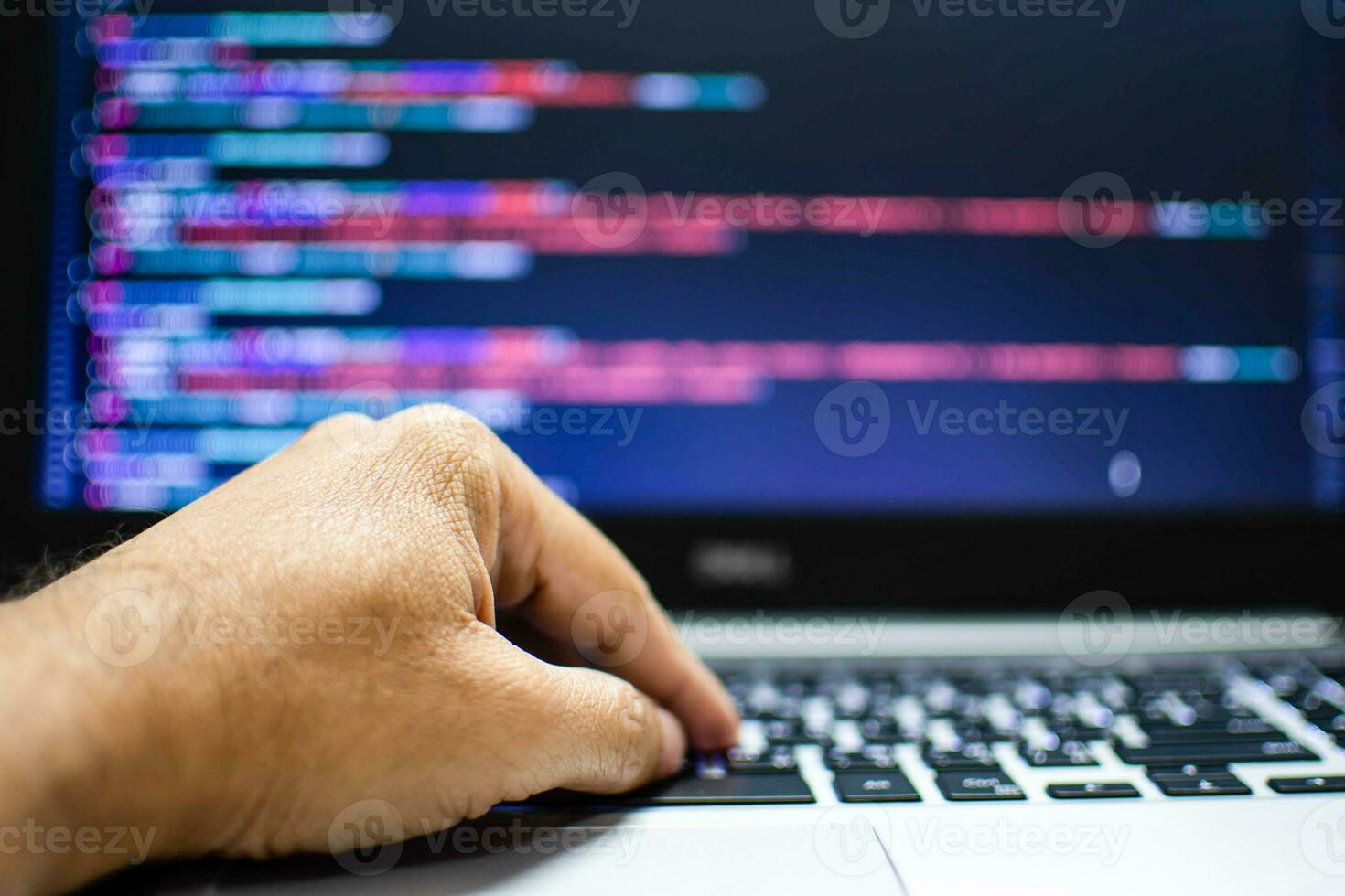 The programmer's hand is writing the source code. Programmers write programs for use with internet business services. The programming code displayed on the laptop screen. Closeup, Blurred background photo