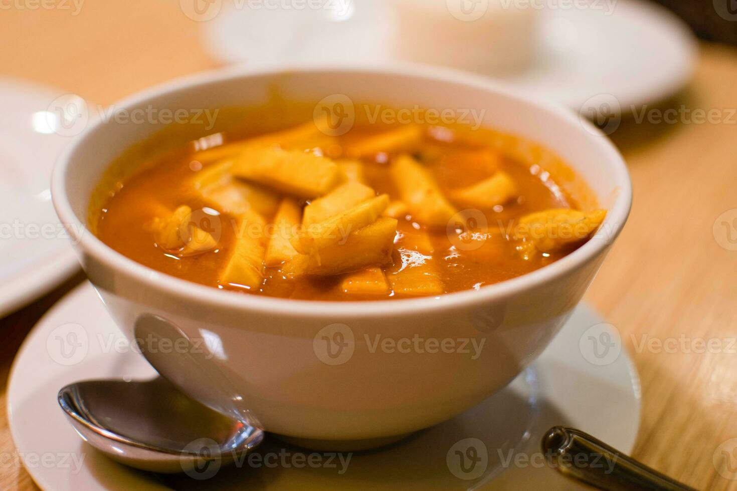 Slope view. Yellow curry, or sea fish sour curry with coconut shoots. The food of Thai people is popular to eat. A white cup of curry is placed on a wooden table in a local restaurant. Closeup. photo