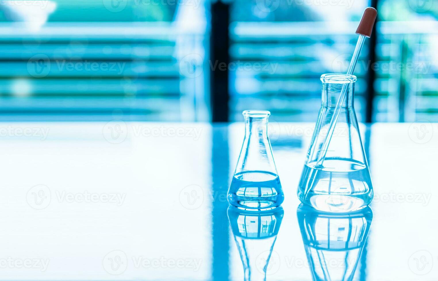 Chemistry experiment concept in science laboratory Two science flasks of different sizes contain different chemicals on white desk. nobody. Copy space on right for design. Blurred background. Close up photo