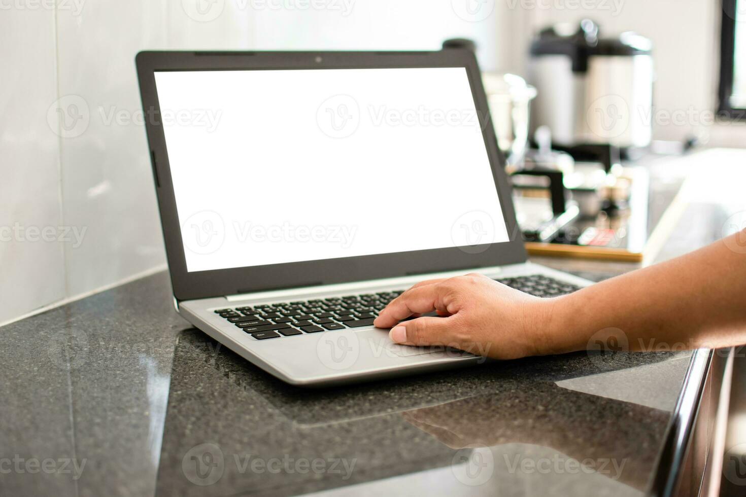Closeup, A woman's hand is typing on a laptop keyboard to search out how to cook. notebook computer white screen on the table. Has a pot on the gas stove. Blurred background, moke up, clipping path photo