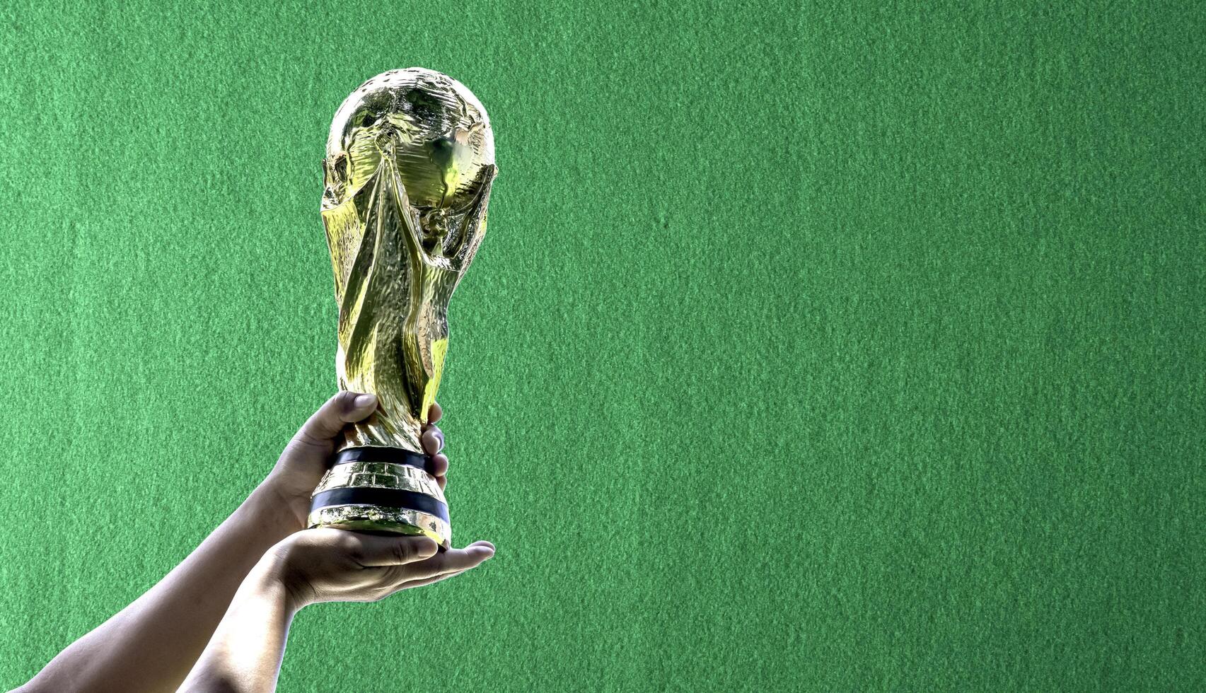 World Cup with green frieze background. hand holding a World Cup winner trophy. The concept for World Cup in Qatar. Copy space on left for design photo