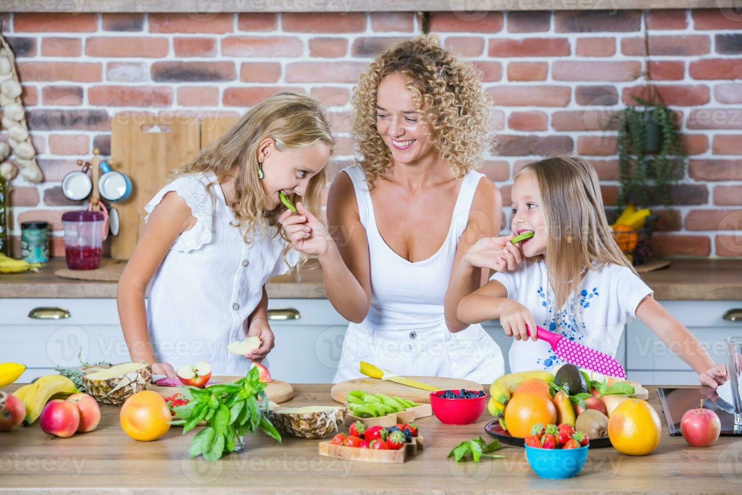 Mother and daughters cooking together in the kitchen. Healthy food concept. Portrait of happy family with fresh smoothies. photo