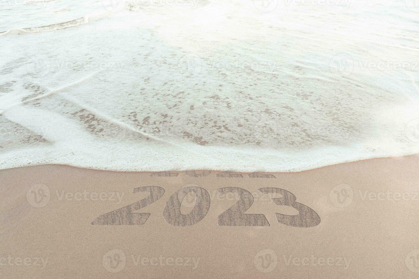 change new year of 2023 on sand of beach. New Year 2023 Concept. inscription is a 2023 number on sand beach. Sandy beach and sea wave beautiful background. Write letters by hand on the beach. photo