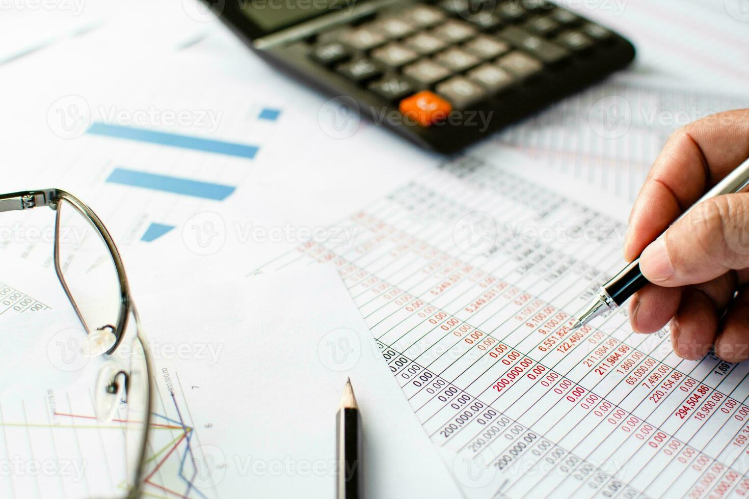 Financial accounting, work at home, Close-up Man's hand holding a pen examining accounting numbers. Numbers on paper and calculator, Many numbers, graph, pencil, glasses on paper, Blurred background. photo