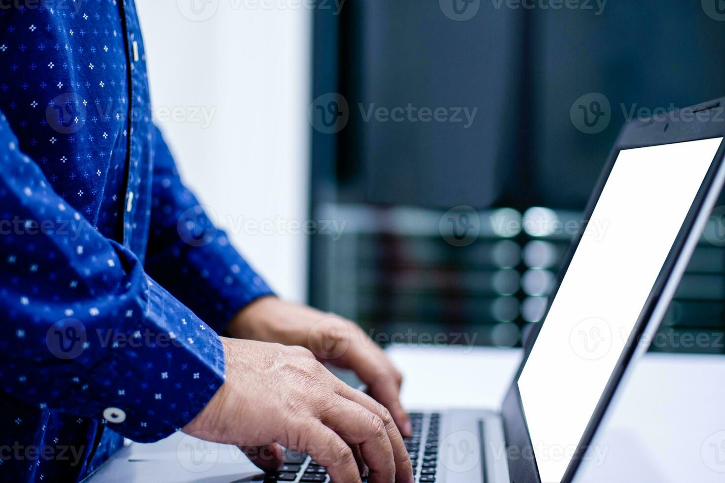 de cerca, personas trabajo hogar blogger un hombre en pie y mecanografía un documento con un cuaderno computadora en un blanco mesa en el vivo habitación a hogar. blanco pantalla es blanco para diseño, burlarse de arriba, recorte camino. foto