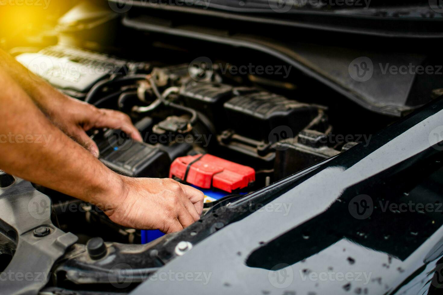 Closeup, The hands of a male technician are using a tool to replace the car battery, parked at home. Black car, the battery is damaged. Man is checking the battery of a black car with no power. photo