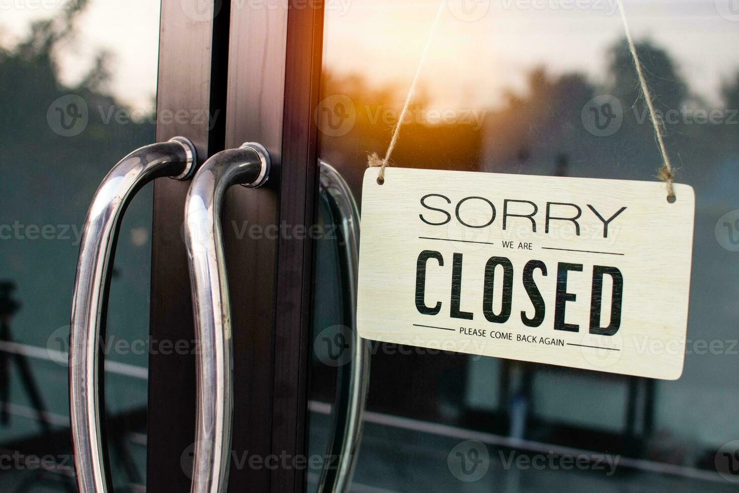 The board hung in front of the glass door of the coffee shop had a  message sorry and closed. Light from the soft sun in the morning was bright as the background. Reflection from nature, sky, trees photo