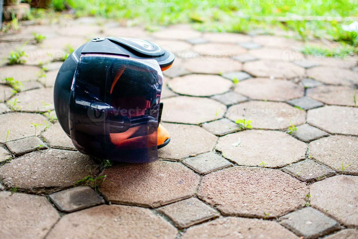Black motorcycle helmet lies at an angle on the roadway from an accident, take close-up photography, the blurred background with green grass and has copy space on the right for put text photo